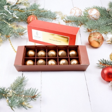 Ésophy box of 10 gold Christmas Pralines displayed with festive fir branches and holiday ornaments; luxury chocolate gift. Luxury Ésophy Christmas Chocolate Pralines with Decorations